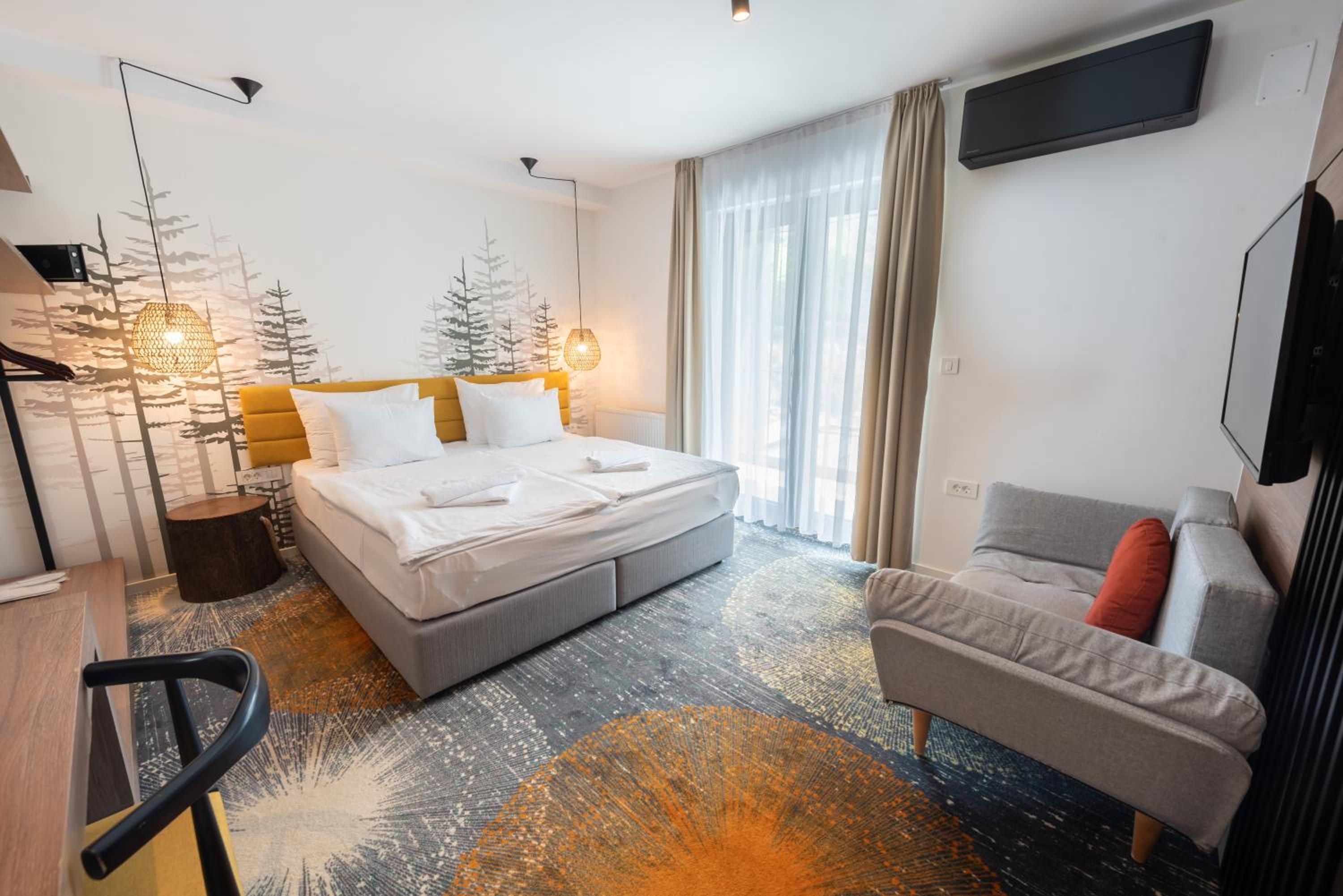 Una habitació d'hotel moderna amb un llit gran, un sofà gris, una taula de treball i una televisió penjada a la paret.