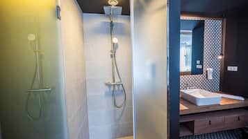 A modern bathroom with a glass shower enclosure, a separate showerhead, and a vanity with a sink and mirror.