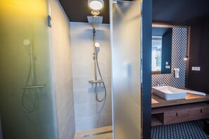 A modern bathroom with a glass shower enclosure, a separate showerhead, and a vanity with a sink and mirror.