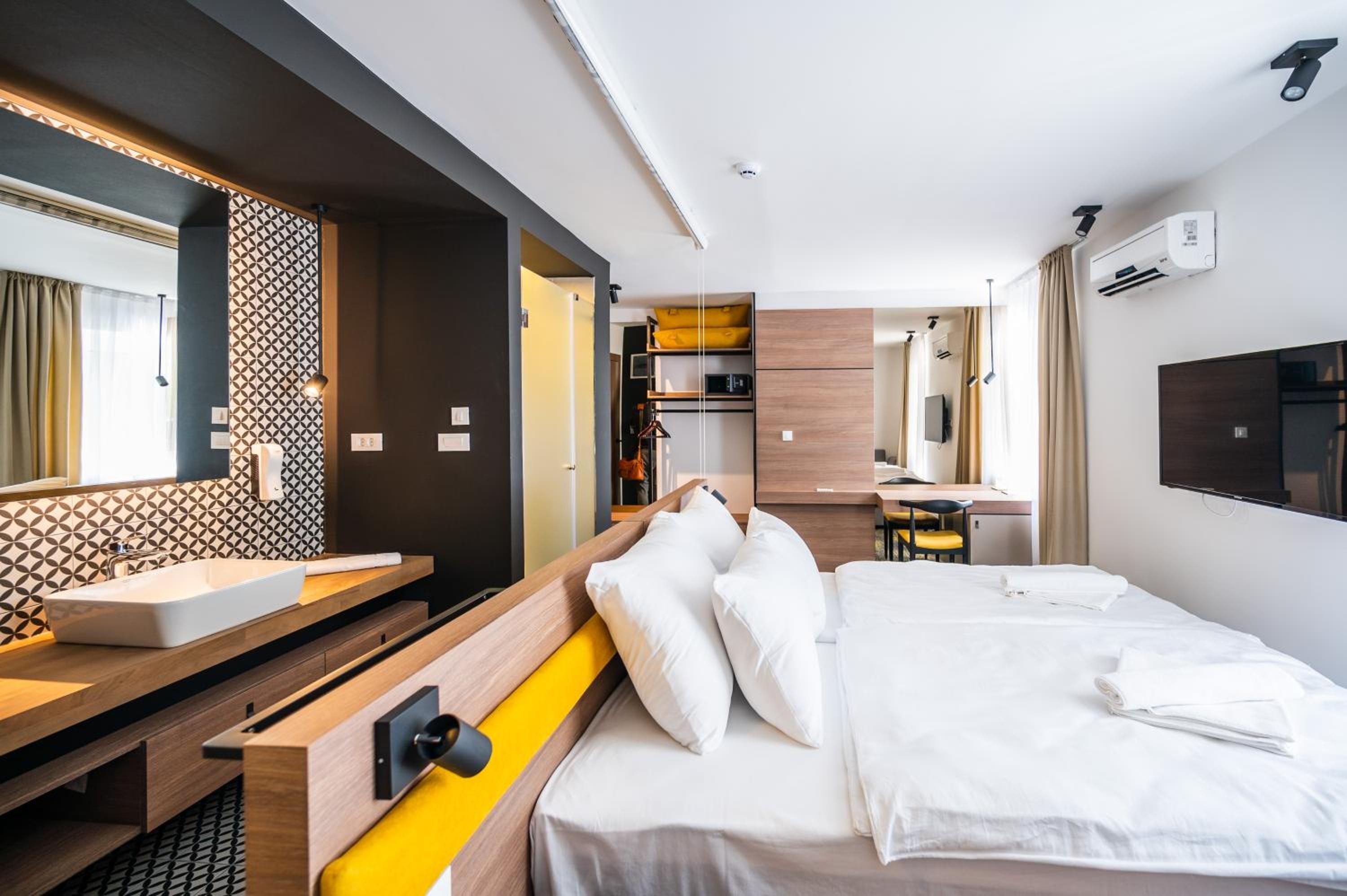 A hotel room with a bed, a bedside table, a mirror, a sink, and a wardrobe.