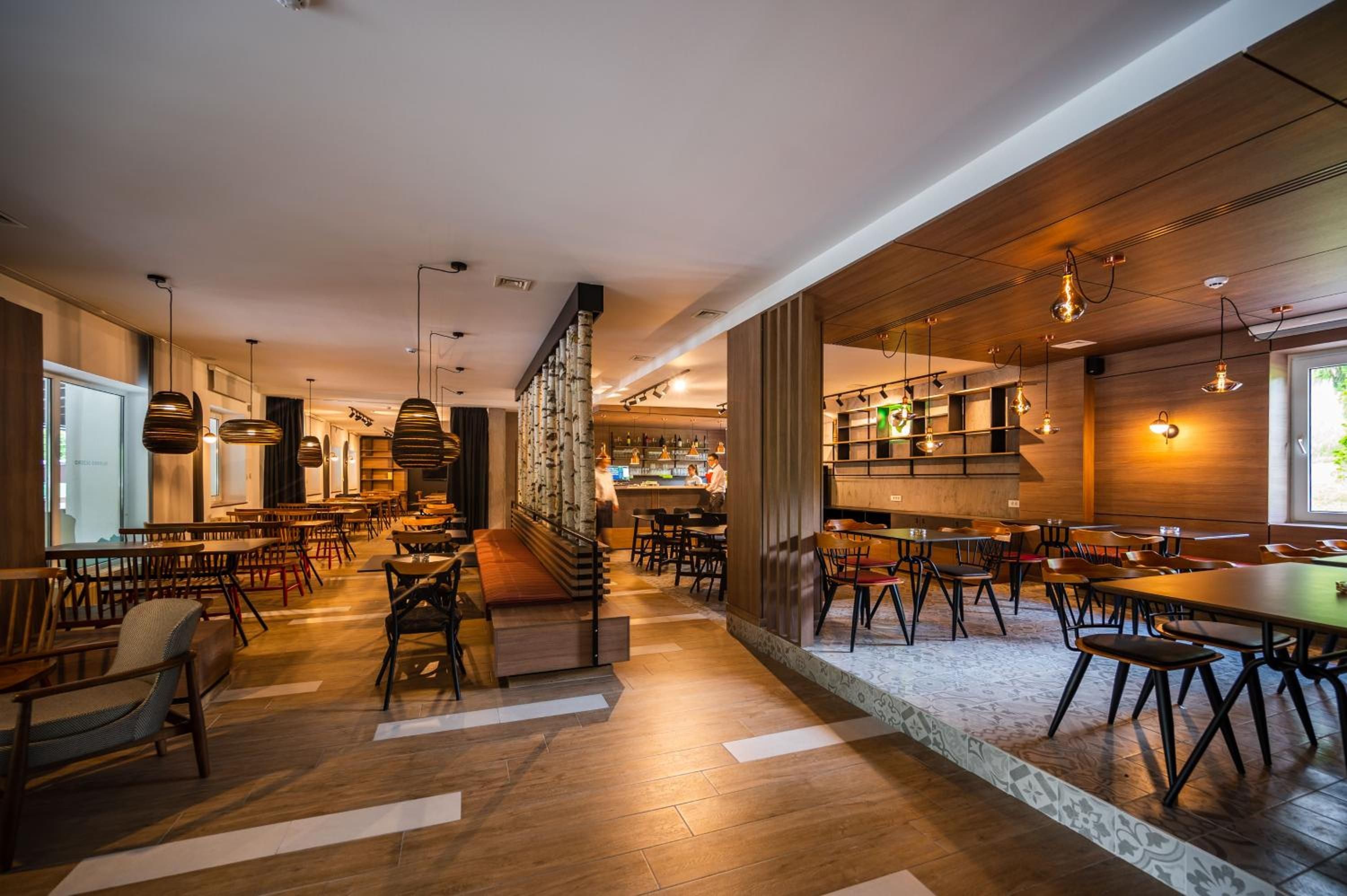 A modern interior with wooden flooring, multiple seating areas, and a bar/lounge area.
