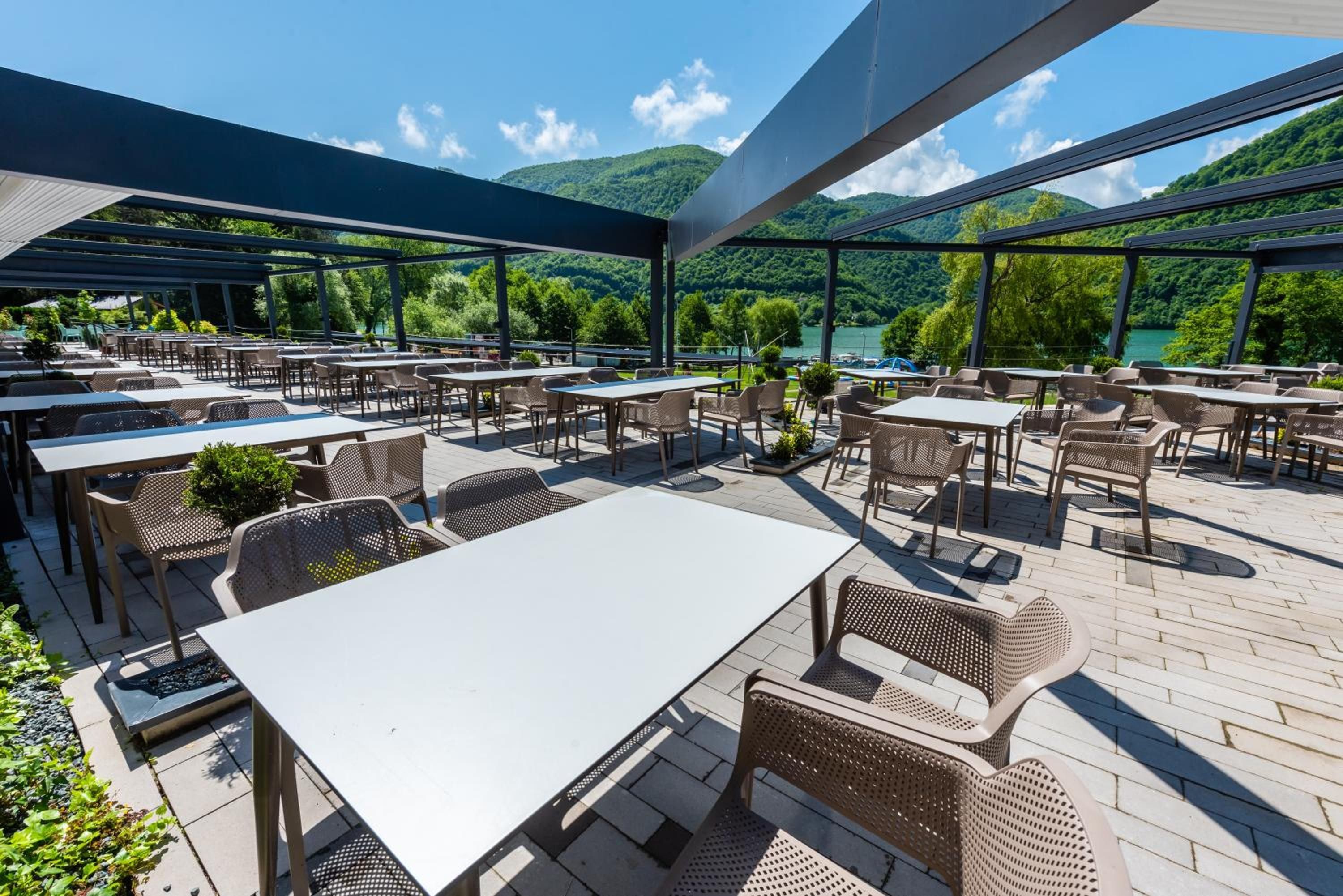 An outdoor patio area with tables and chairs, overlooking a lake and hills.