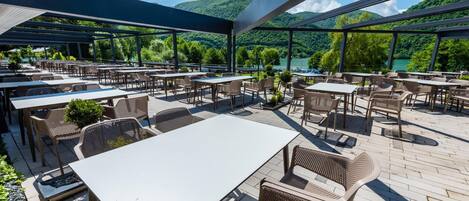 An outdoor patio area with tables and chairs, overlooking a lake and hills.
