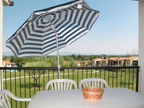 Uma varanda com um guarda-sol listrado, cadeiras brancas, uma mesa e um cesto.