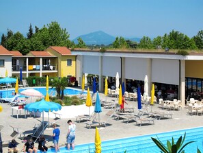 Ein Poolbereich mit Liegestühlen und Sonnenschirmen, ein Gebäude mit Balkonen und ein Berg im Hintergrund.