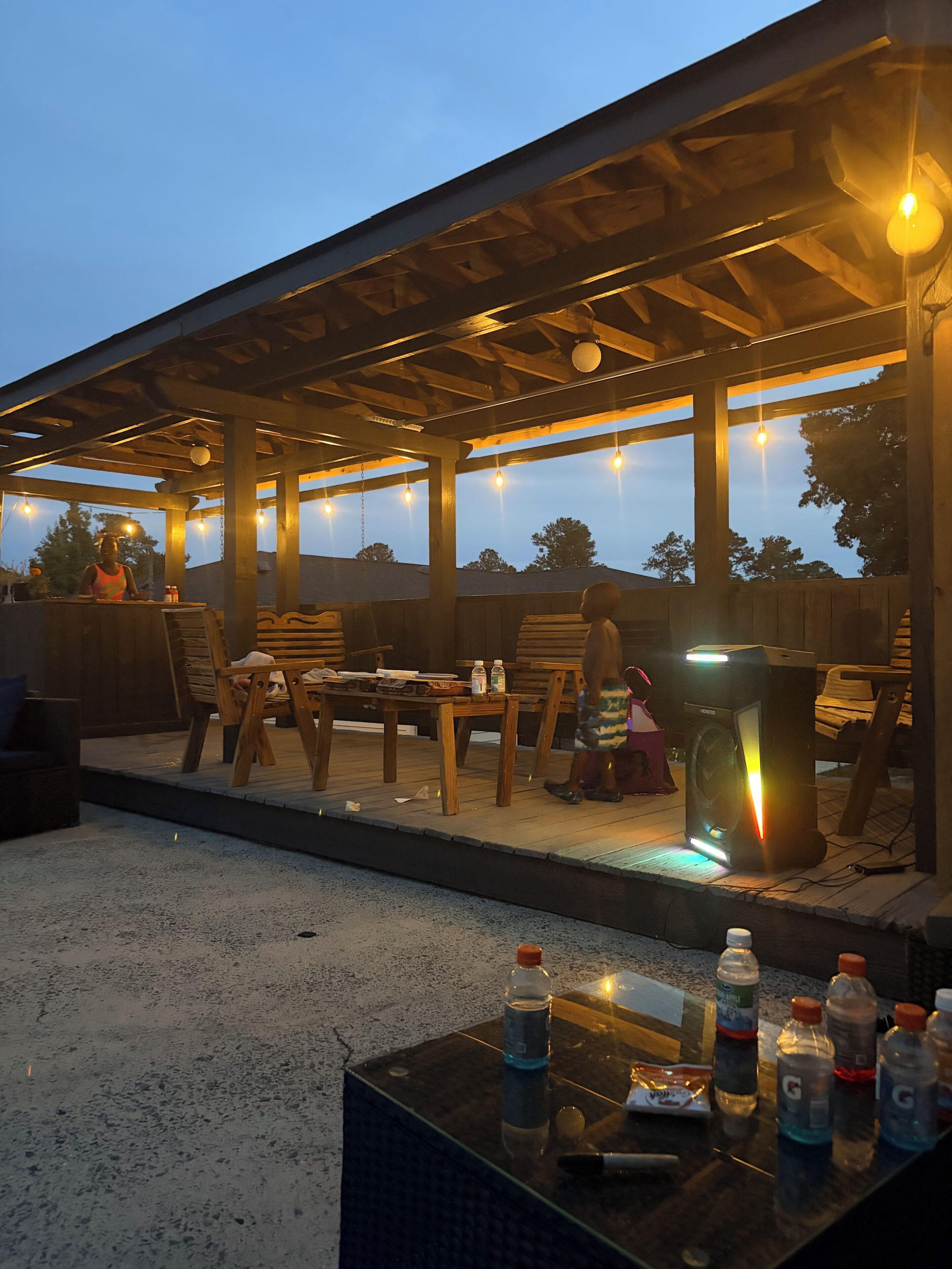 An outdoor patio area with wooden furniture, string lights, and a speaker.