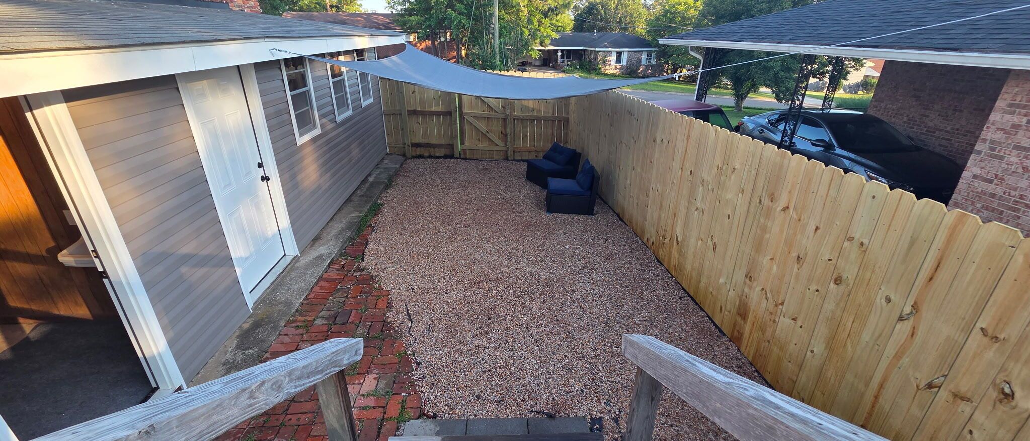 A covered outdoor area with a wooden fence, a gravel path, and two black outdoor sofas.