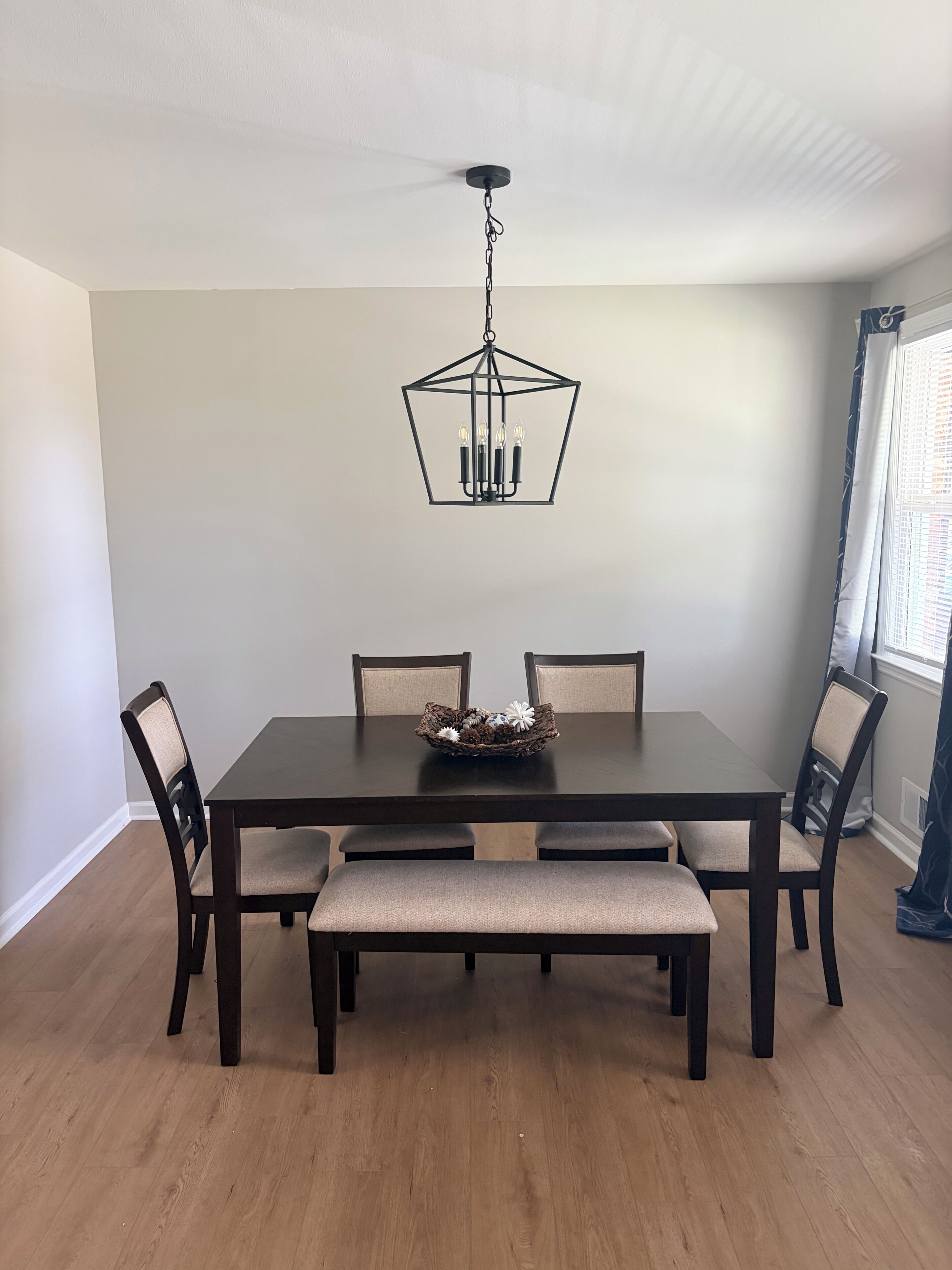 Une salle à manger avec une table en bois foncé, quatre chaises, un banc et un luminaire suspendu.