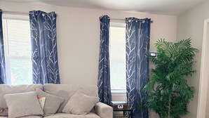 Ein Wohnzimmer mit einem beigen Sofa, einem kleinen Tisch mit einer Pflanze und einem Fenster mit Vorhängen.