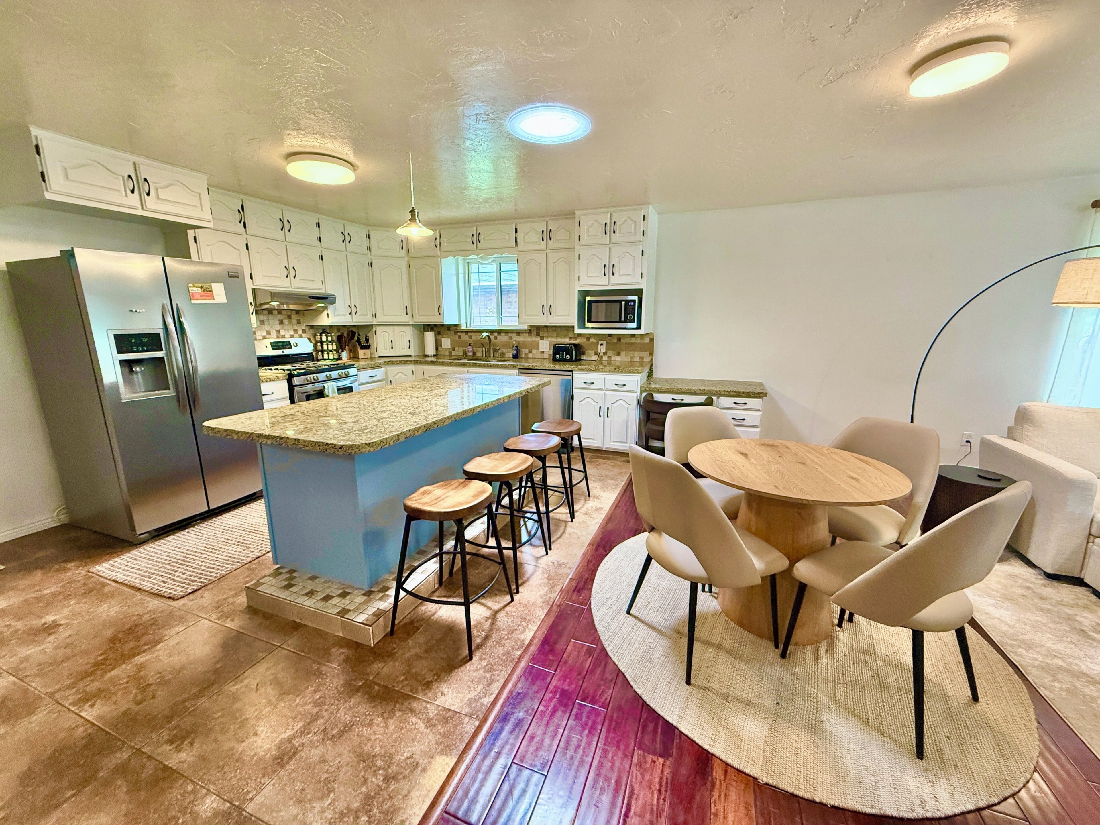 A modern kitchen with a central island, bar stools, a dining table with chairs, and a microwave.