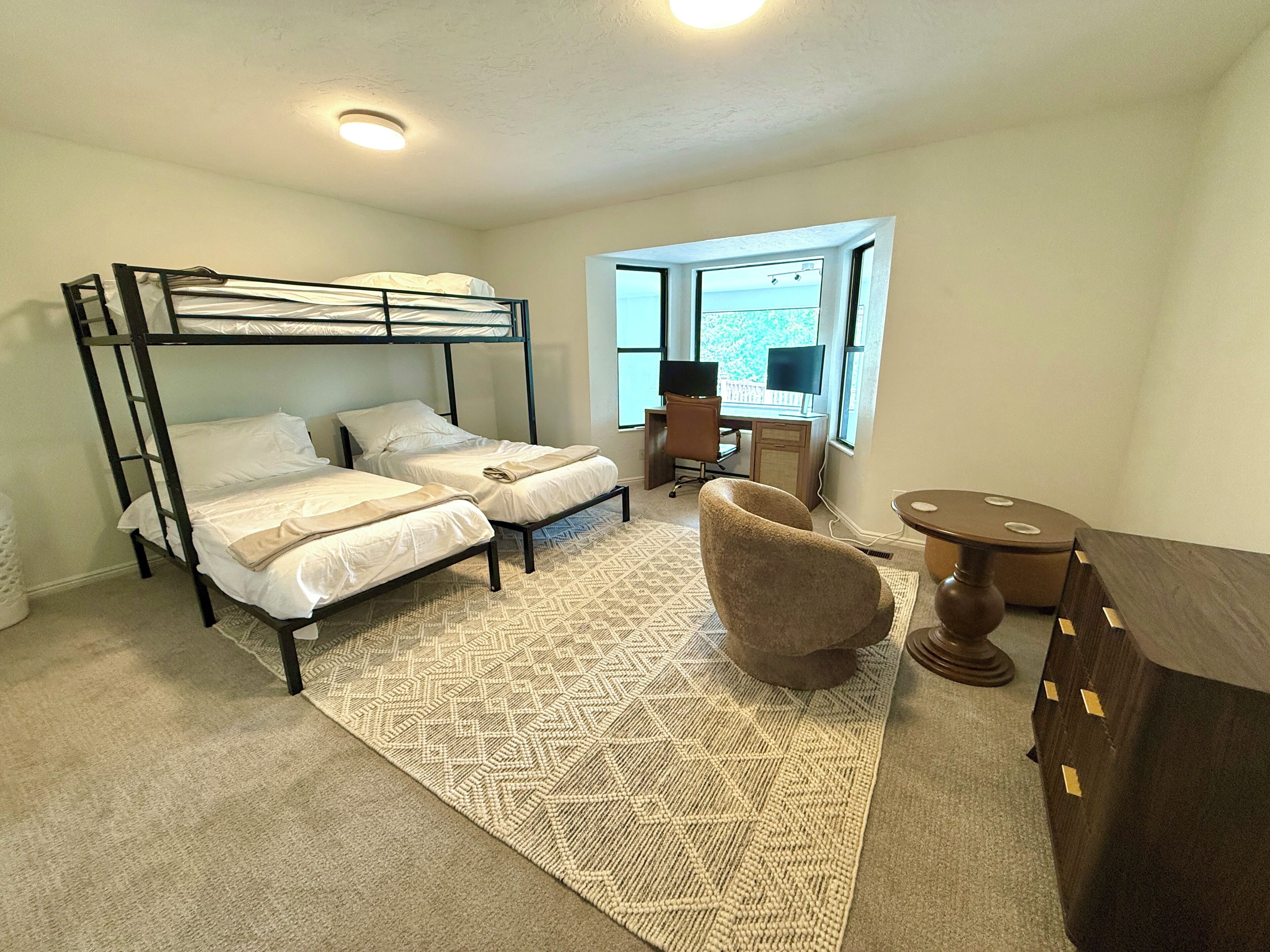 A room with a bunk bed, a desk with a computer, a chair, and a small table.