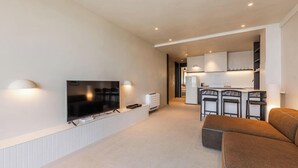 A modern living room with a flat-screen TV, a sofa, and a kitchen area with bar stools. - Casa Sud Luxury 2BR Apartment (Vlorë)