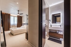 Ein modernes Hotelzimmer mit einem Bett, einem Deckenventilator, einem Badezimmer mit Waschbecken und Spiegel sowie Blick ins Freie.
