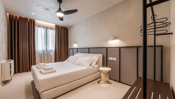 A modern bedroom with a bed, a ceiling fan, a bedside table, and a wall-mounted towel rack. - Casa Sud Luxury 2BR Apartment (Vlorë)