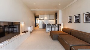 A modern living room with a flat-screen TV, a sofa, and a dining area with chairs. - Casa Sud Luxury 2BR Apartment (Vlorë)