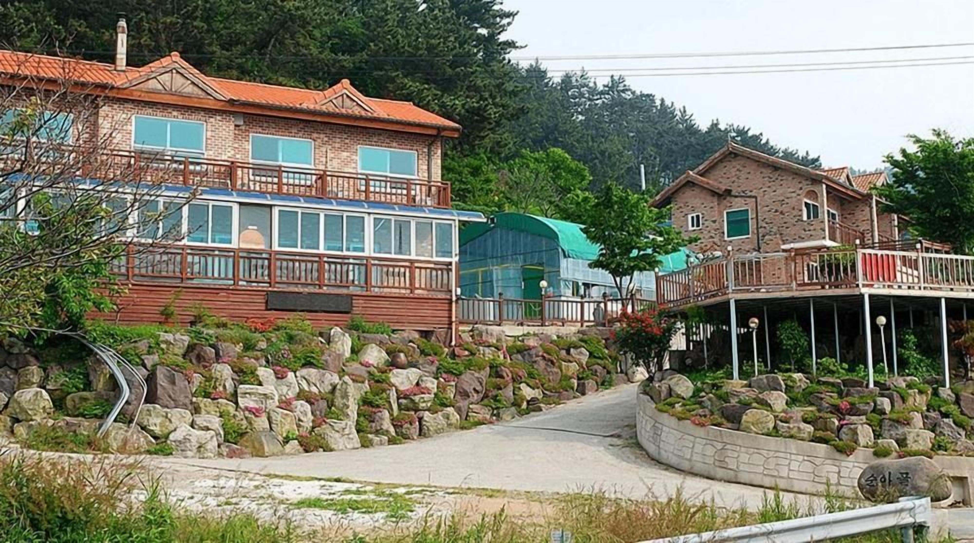 A residential area with a stone pathway leading to a wooden deck, surrounded by a stone wall and greenery.