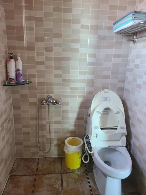 A small bathroom with a toilet, a shower, and a shelf with toiletries. - Yeonggwang Chohyeon Pension (Yeonggwang)