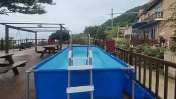 A rectangular swimming pool with a ladder, surrounded by a wooden deck with picnic tables.