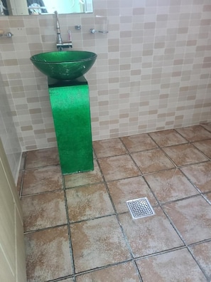 A bathroom with a green sink, tiled walls, and a drain.