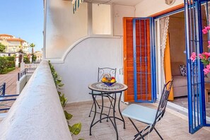 A balcony with a table and chairs, a bowl of fruit, and a view of the street. - Pink Buganvilla Lodging (Torrevieja)