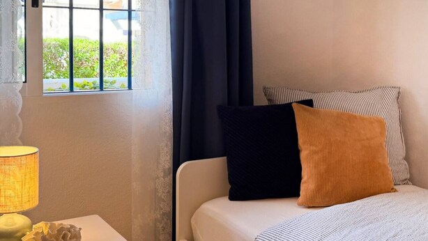 Quarto de hotel com cama, mesa de cabeceira e luminária, além de janela com cortinas.