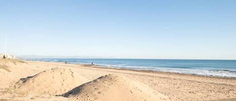 A beach with a wooden boardwalk leading to the shore, clear skies, and a calm sea.