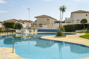 Ein Swimmingpool mit glatter, blauer Wasseroberfläche, umgeben von einem weißen Zaun, neben einer Reihe von Gebäuden mit ähnlicher Architektur.