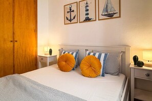 A bedroom with a bed, two bedside tables, a nightstand, a wooden wardrobe, and wall art. - Pink Buganvilla Lodging (Torrevieja)