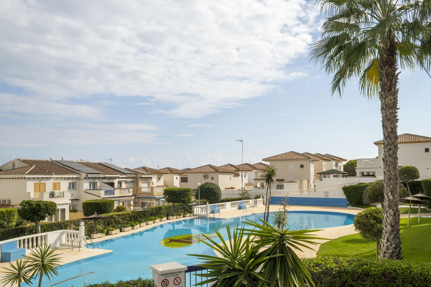Ein Wohngebiet mit Swimmingpool, Häusern mit Ziegeldächern und Palmen.