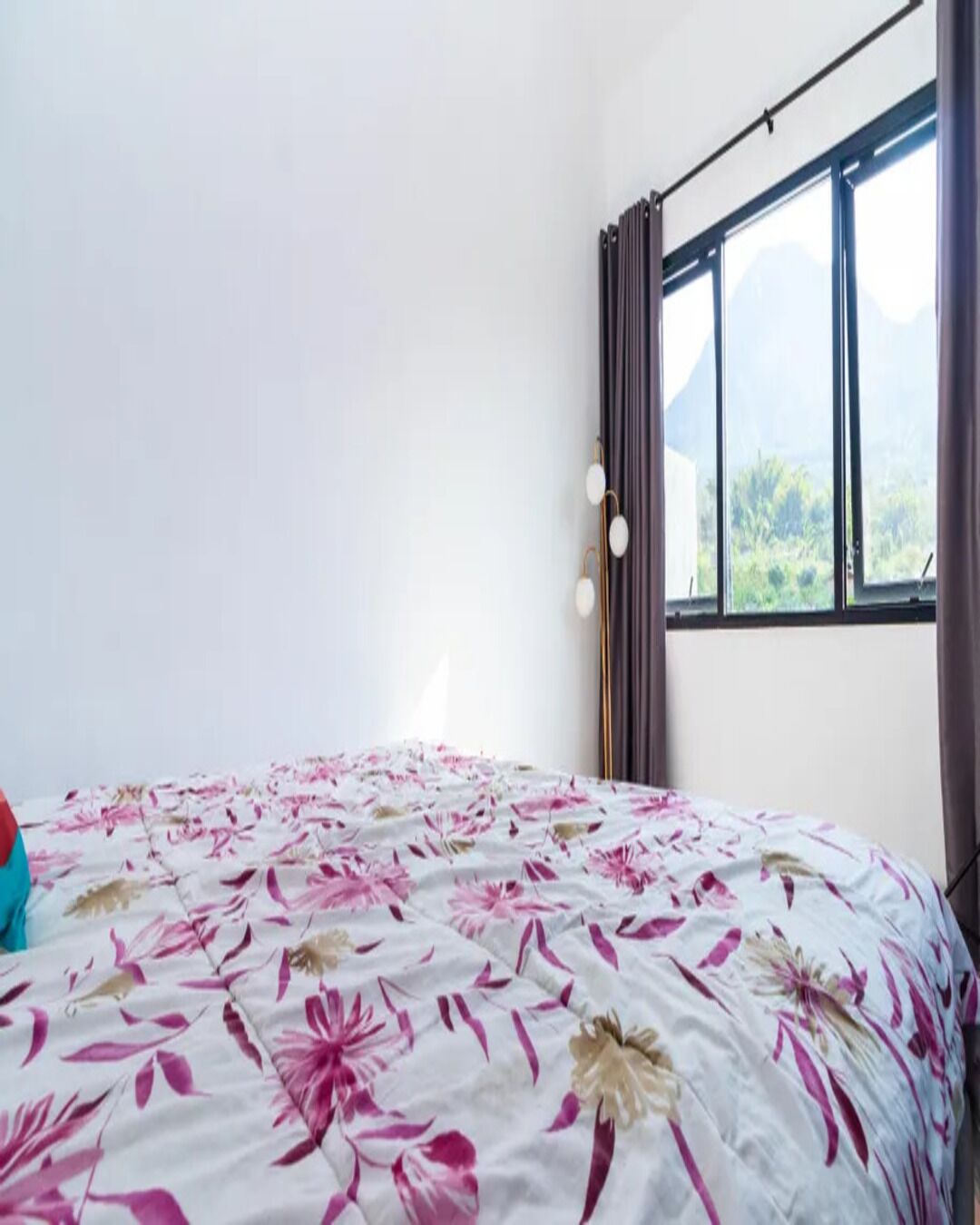 Ein Schlafzimmer mit einem Bett, einem Fenster mit Vorhängen und Blick auf Grünfläche.
