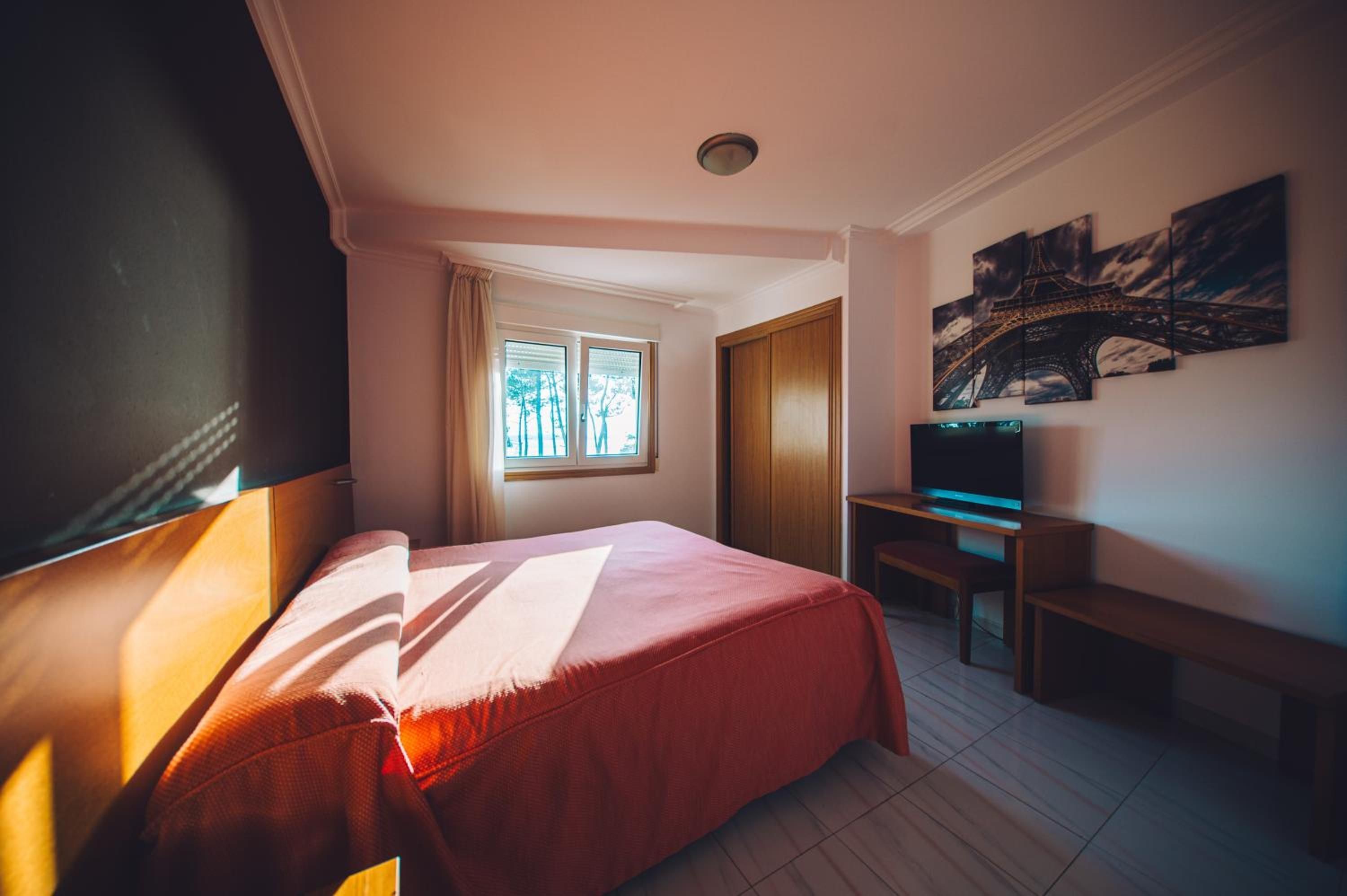 Habitación de hotel con cama, escritorio, televisor y ventana con cortinas.