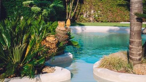 A tranquil pool with clear blue water, surrounded by lush greenery and palm trees. - Hotel Dinajan (Vilanova de Arousa)