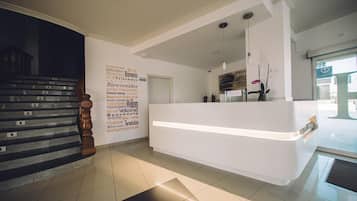 Zona de recepción de un hotel con diseño moderno, una mesa de recepción, una escalera y una pared con mensajes de bienvenida en varios idiomas.