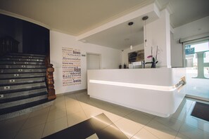 Un espace d’accueil d’hôtel au design moderne, comprenant un comptoir d’accueil, un escalier et un mur orné de messages de bienvenue dans plusieurs langues.