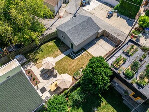 Una propiedad residencial con una casa independiente, un patio trasero cercado y una zona de patio con mobiliario exterior.