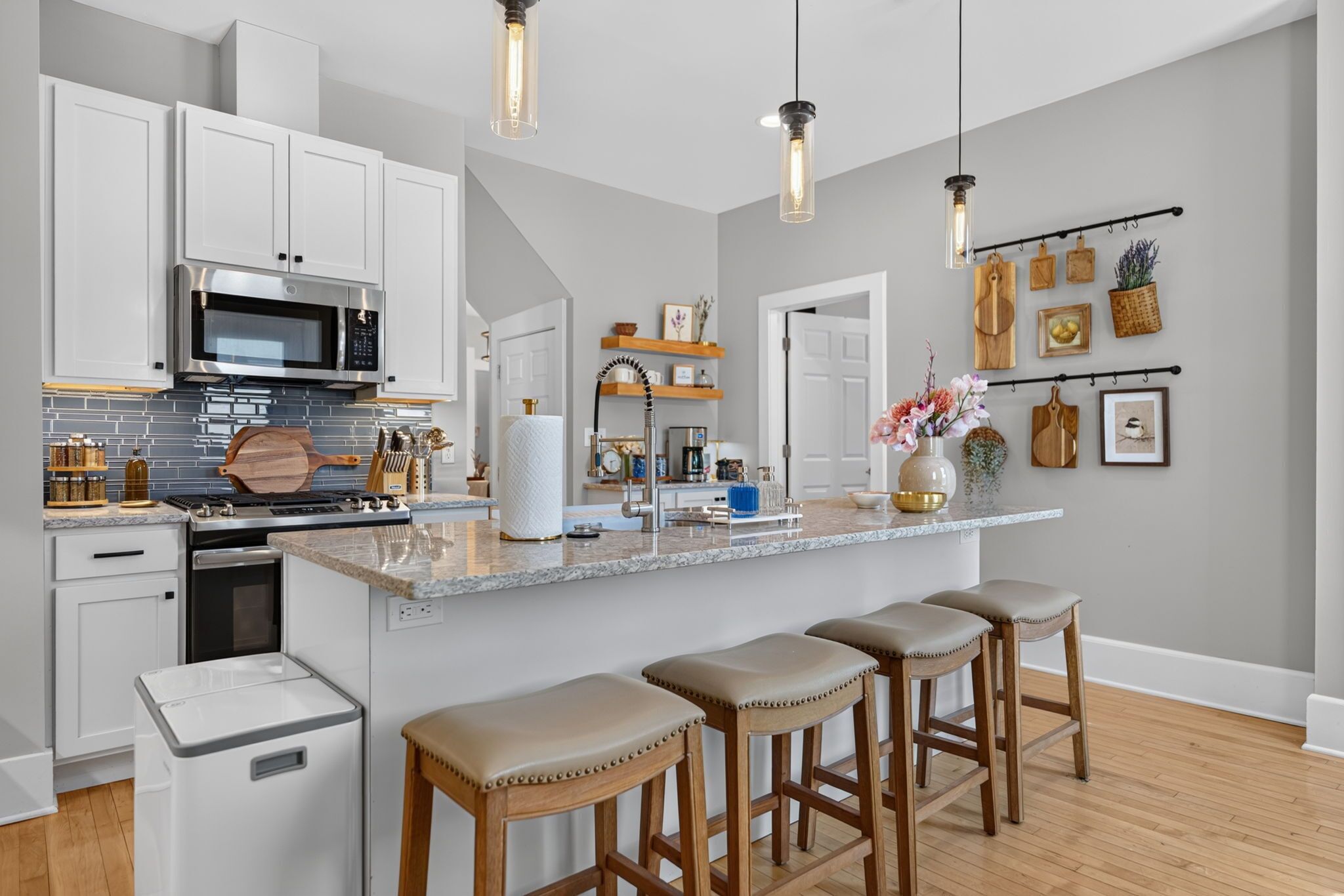 A modern kitchen with white cabinetry, a central island with bar stools, a microwave, and a stainless steel oven.