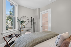 A bedroom with a bed, a window, a dresser, a mirror, and a door. - Lavender Hill Skyline - Sleeps 12 - City Views (Milwaukee)