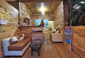 A reception area with a wooden interior, a reception desk, a couch, and a poster board with information. - Jerogadung House (Ubud)