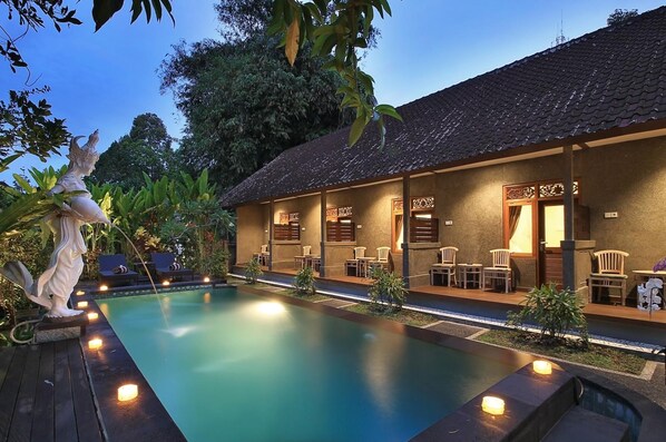 A poolside area with a covered seating area and a statue. - Jerogadung House (Ubud)