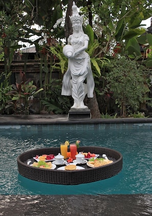 A statue in a garden setting with a floating dining table by a pool. - Jerogadung House (Ubud)