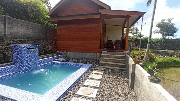 Ein Schwimmbecken mit Fliesenrand, eine Holzhütte mit Veranda und eine Steinmauer.