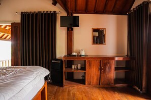 A bedroom with a bed, a desk with a mirror, a television, and a heater. - Nea Cottage Lombok (Tetebatu)