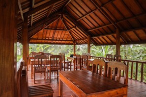 An outdoor wooden pavilion with tables and chairs, surrounded by lush greenery. - Nea Cottage Lombok (Tetebatu)