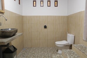 A bathroom with a stone-tiled floor, a white toilet, a sink with a stone basin, and a shower area. - Nea Cottage Lombok (Tetebatu)