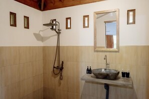 A bathroom with a stone sink, a handheld showerhead, and a mirror above it. - Nea Cottage Lombok (Tetebatu)