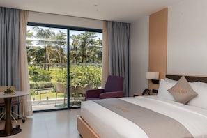 A hotel room with a bed, a chair, a small table, and a balcony with a view of palm trees. - Lugano Resort & Spa - Ultra All Inclusive (Cam Lam)