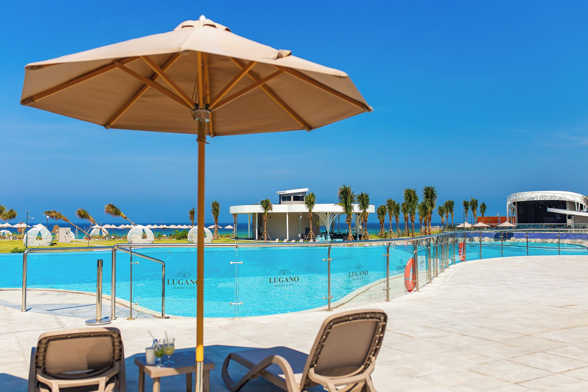 Uma área à beira da piscina com espreguiçadeiras, um guarda-sol e vista clara para o oceano.