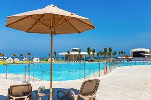 Ein Poolbereich mit Liegestühlen, Sonnenschirm und freiem Blick auf das Meer.
