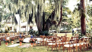 An outdoor seating area with wooden chairs and tables, surrounded by trees with hanging moss. - Hacienda La Armenia - Cottage Hotel (Sopó)