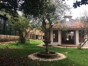 A courtyard with a fountain, a small building with a tiled roof, and a stone wall. - Hacienda La Armenia - Cottage Hotel (Sopó)
